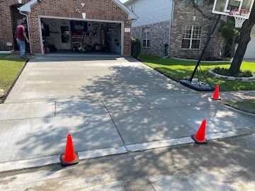 A freshly paved residential driveway with orange traffic cones blocking the entrance.