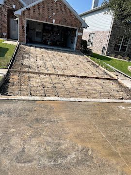 A driveway prep area with wire mesh reinforcement grid laid out over dirt, framed by wooden forms, ready for concrete.