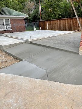 Freshly poured concrete patio and driveway extension next to a brick house and wooden fence.