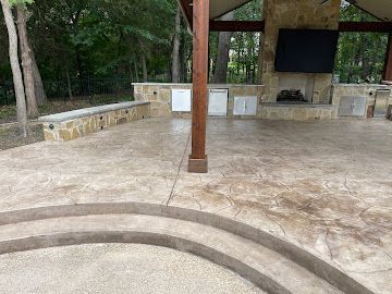 A covered outdoor patio with stamped concrete, a stone fireplace, integrated storage cabinets, and curved steps.