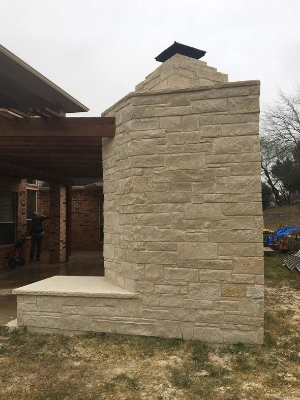 Outdoor stone fireplace chimney with a covered patio area in the background under a cloudy sky.