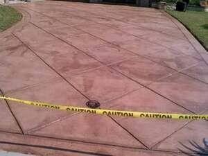 A stamped, reddish-brown concrete driveway with a diamond-pattern design, partitioned by yellow caution tape.