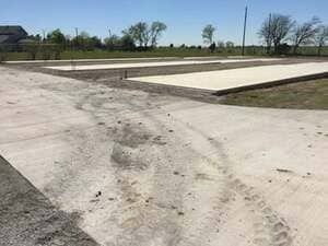 A view of two large, rectangular concrete pads under construction, situated in a field under a clear blue sky.