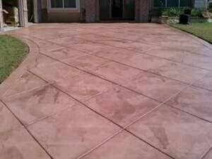 A stamped concrete driveway featuring a reddish-brown, diagonal grid pattern leading to a home entrance.