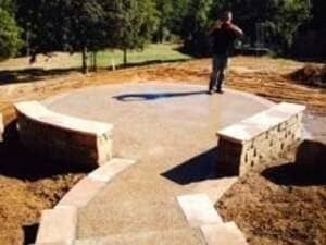 A person stands on a circular stone patio featuring two curved stone bench walls and steps leading up to it.