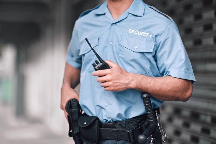 A security guard is holding a walkie talkie in his hand.