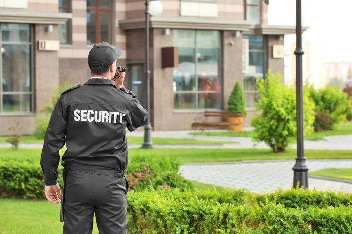 A security guard is talking on a cell phone in front of a building.