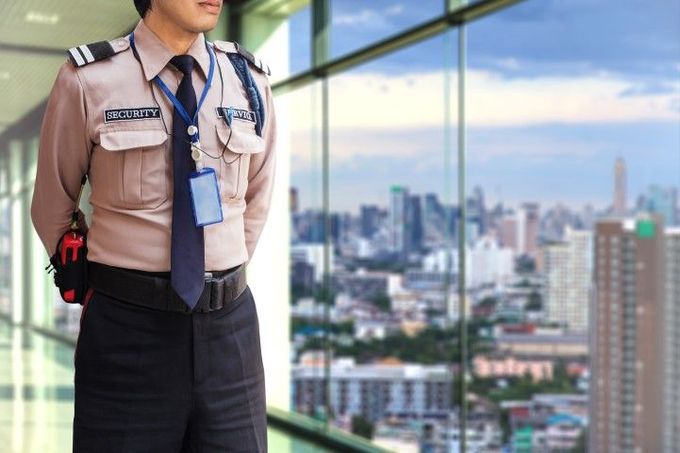 A security guard is standing in front of a window looking out over a city.