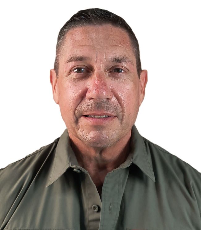 Man in olive green collared shirt smiles at camera, against white backdrop.