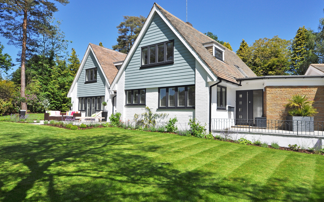 House with blue siding, black shutters, and well-manicured green lawn on a sunny day.