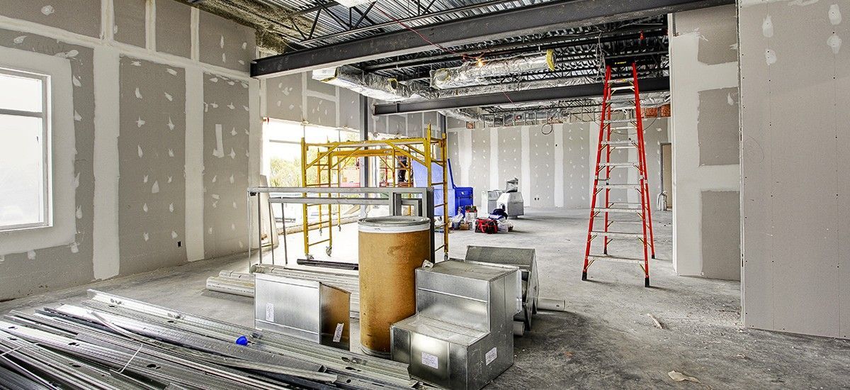 A large room is being remodeled with drywall and a ladder.