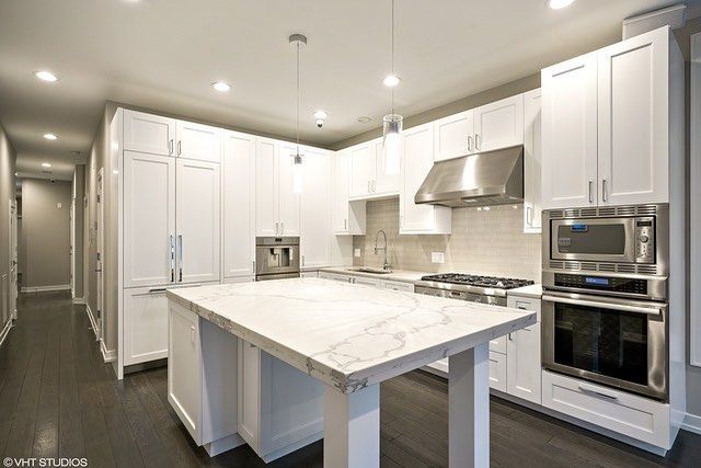 Modern white kitchen with marble island, stainless steel appliances, and bright recessed lighting
