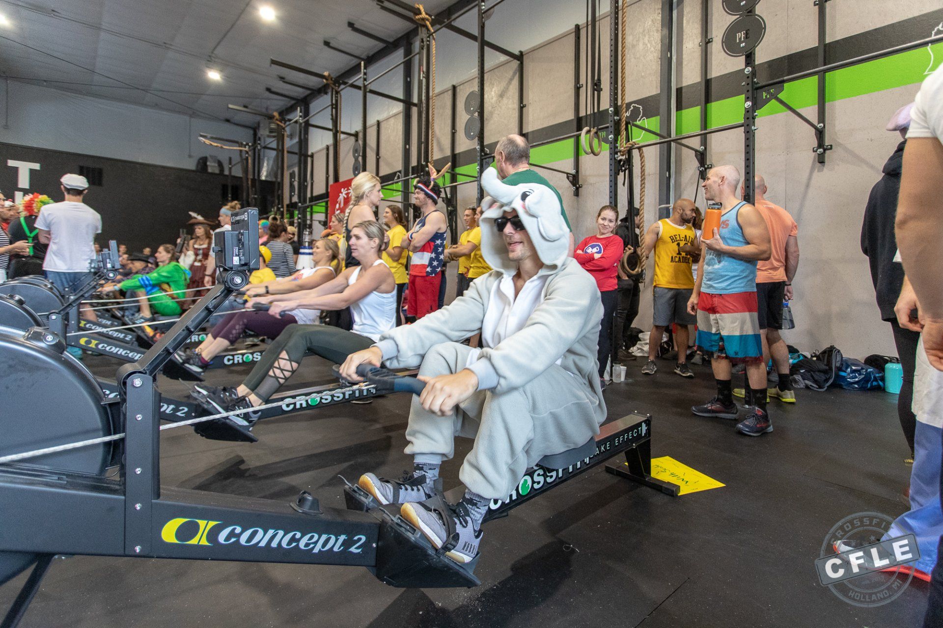 A man in a unicorn costume is riding a rowing machine in a gym.