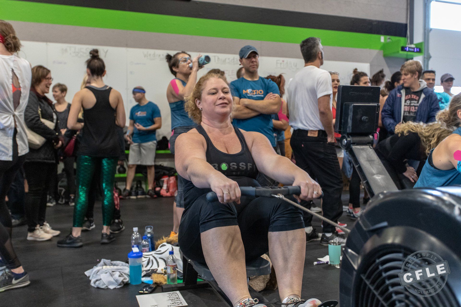 A woman is rowing a rowing machine in a gym while a group of people watch.