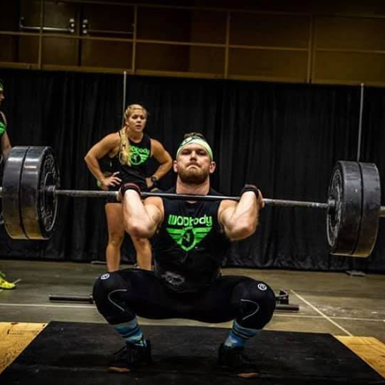 A man is squatting down while holding a barbell.