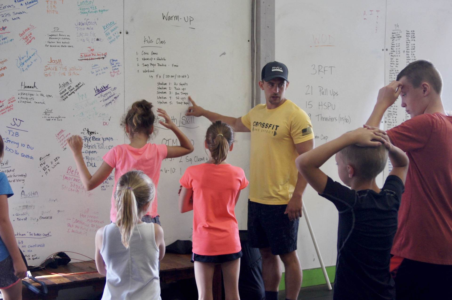 A man in a yellow shirt with the word might on it stands in front of a group of children