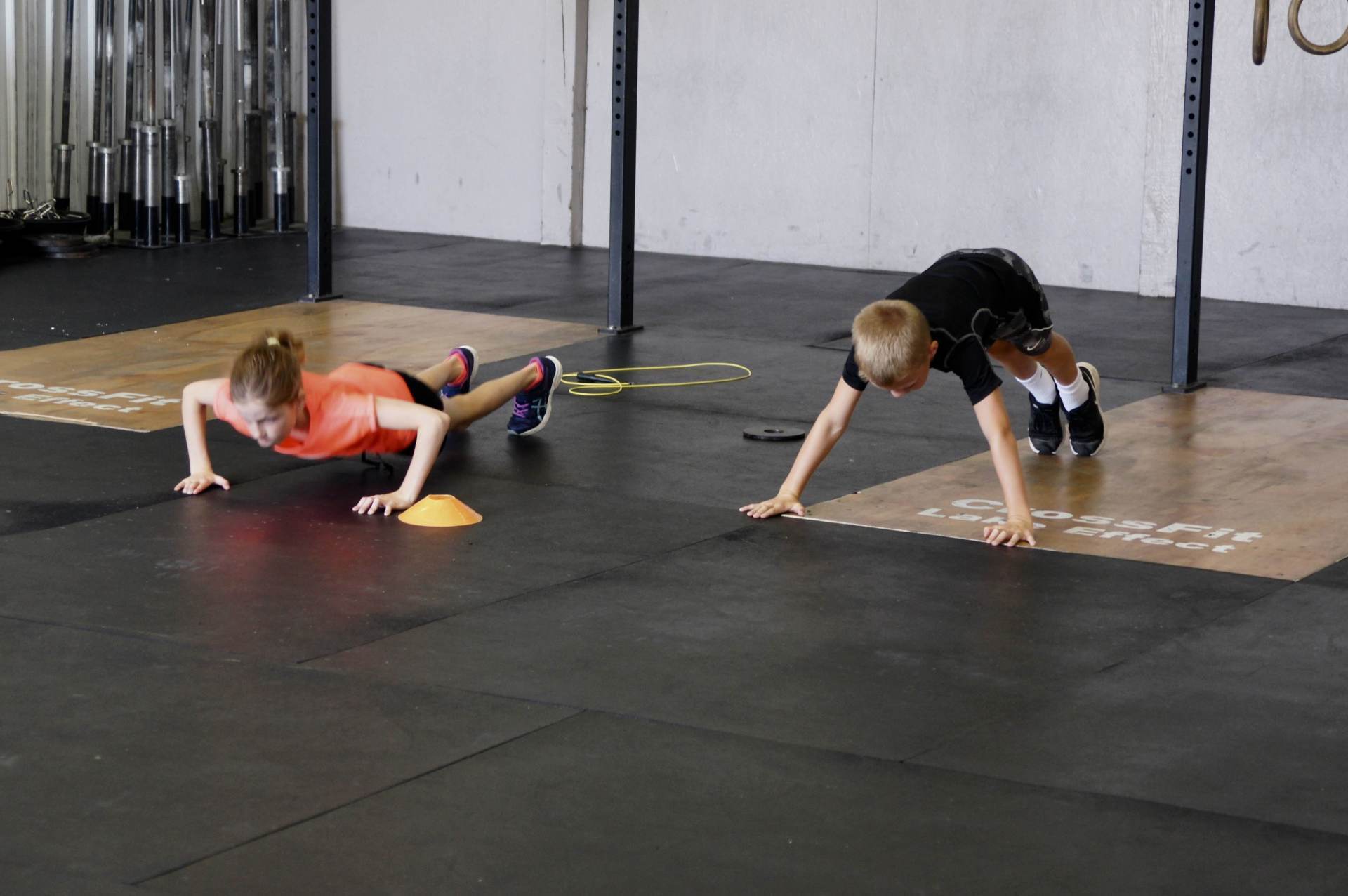 A boy and a girl are doing push ups in a gym.