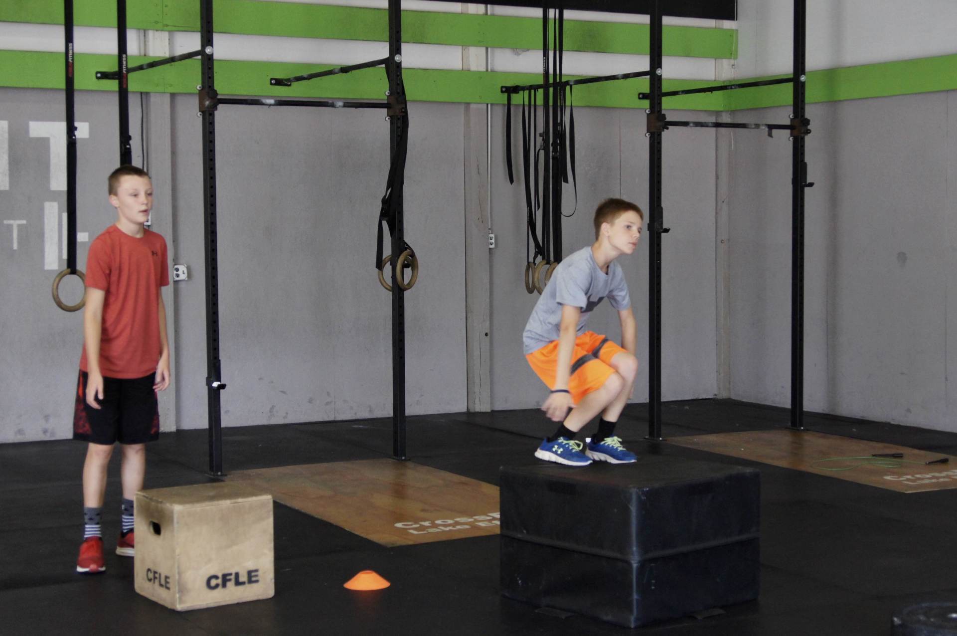 Two young boys are jumping on a box in a gym.