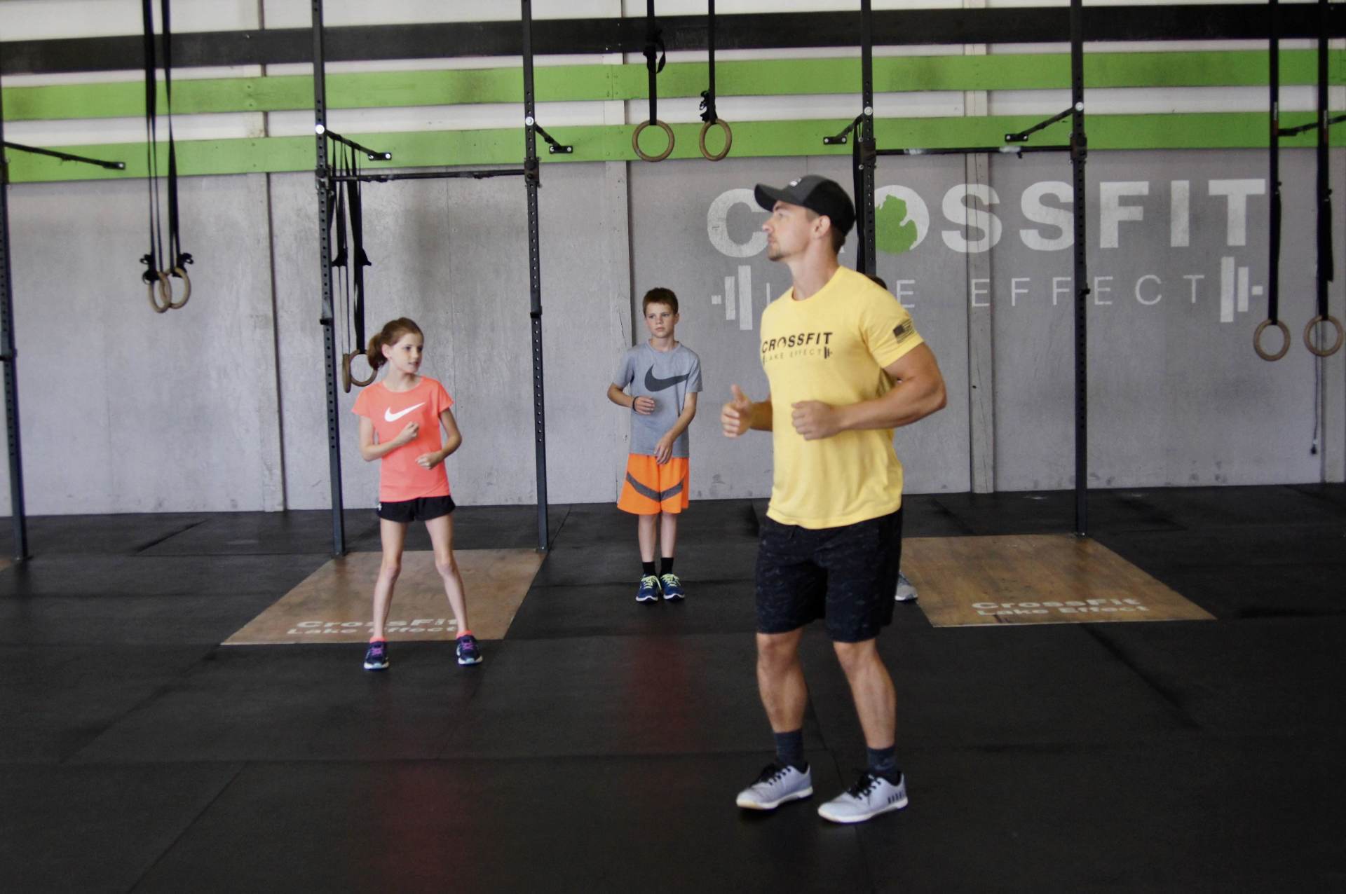 A man in a yellow shirt is standing in a gym with two children.
