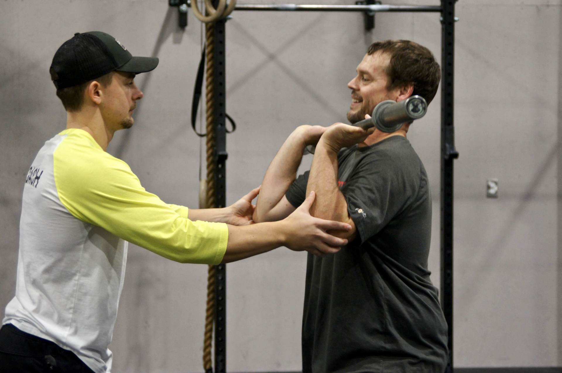 A man is helping another man lift a dumbbell in a gym.