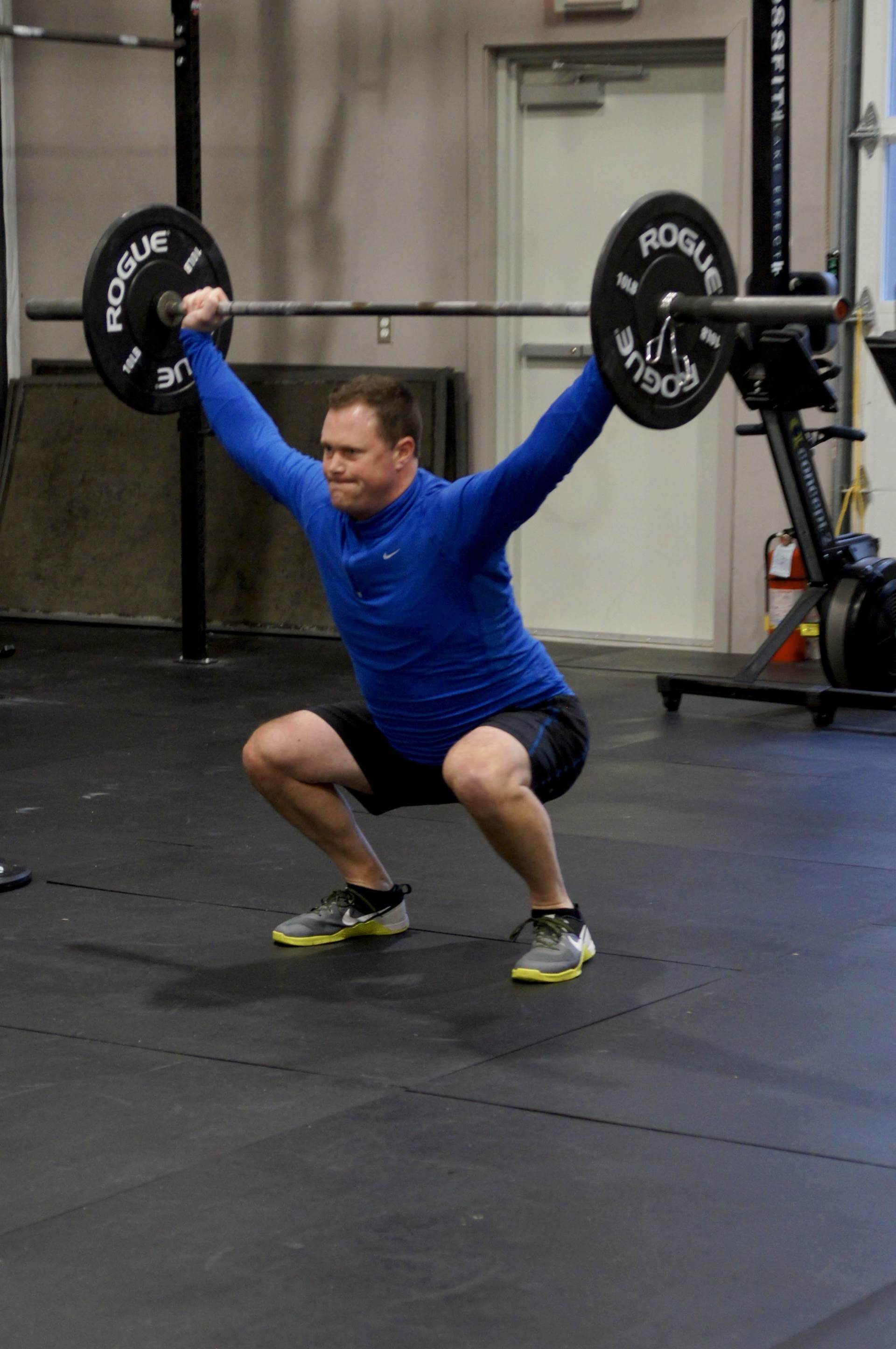 A man is squatting down while holding a barbell over his head.