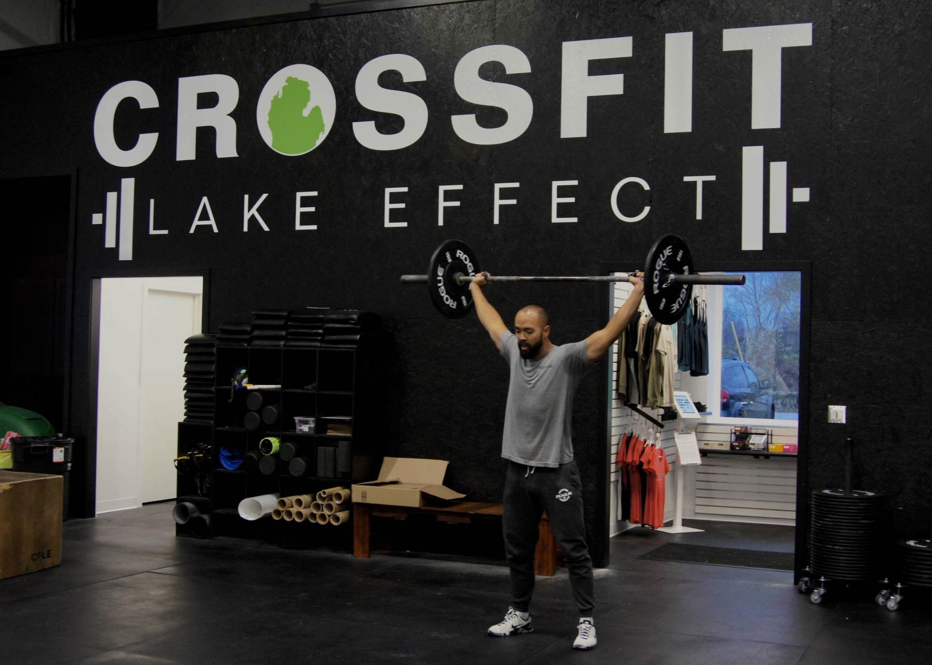 A man is lifting a barbell in front of a wall that says crossfit lake effect