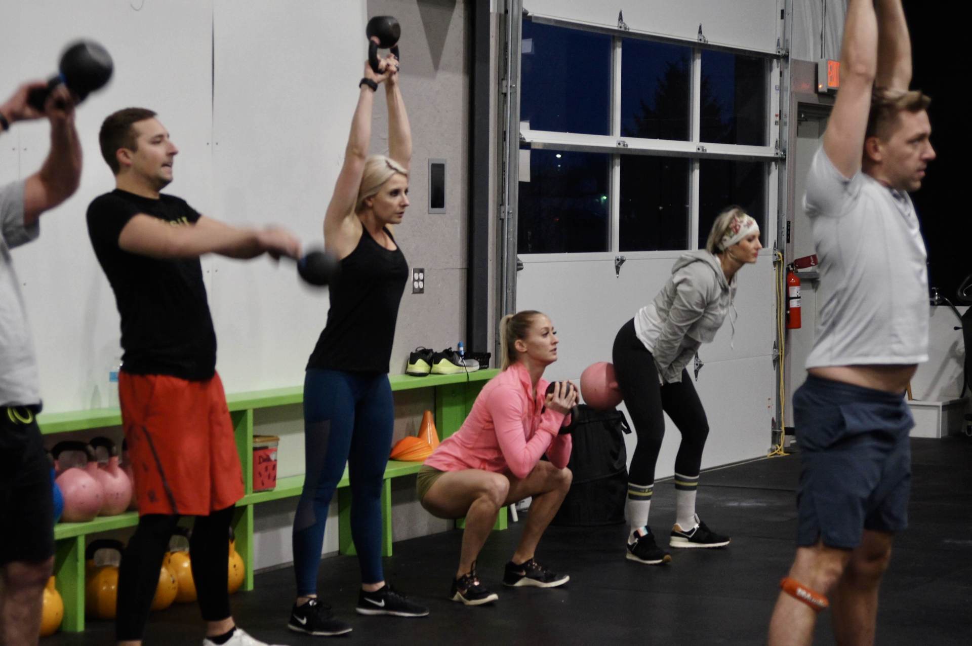A group of people are doing exercises with kettlebells in a gym.