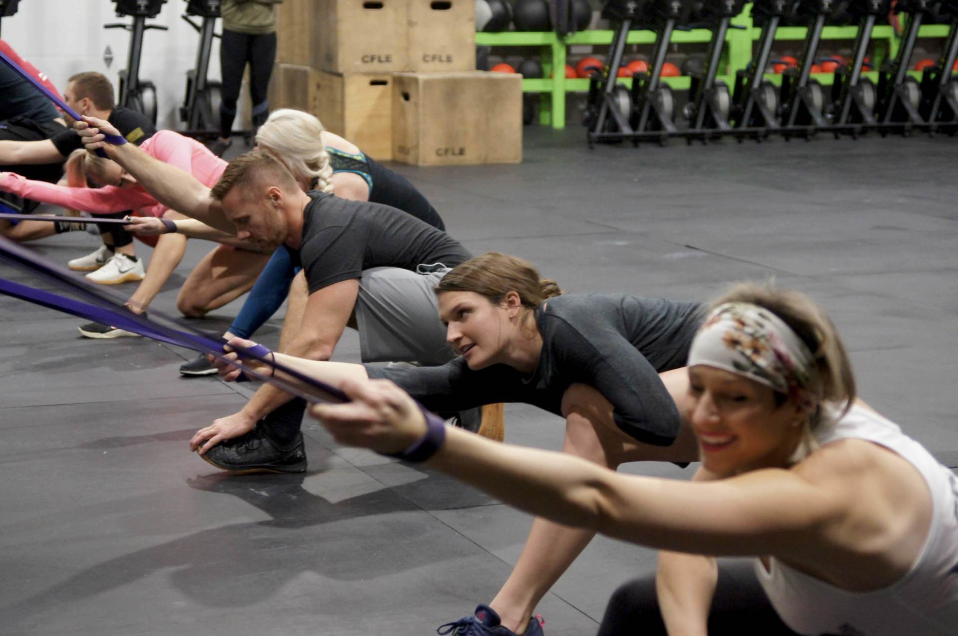 A group of people are doing squats with resistance bands in a gym.
