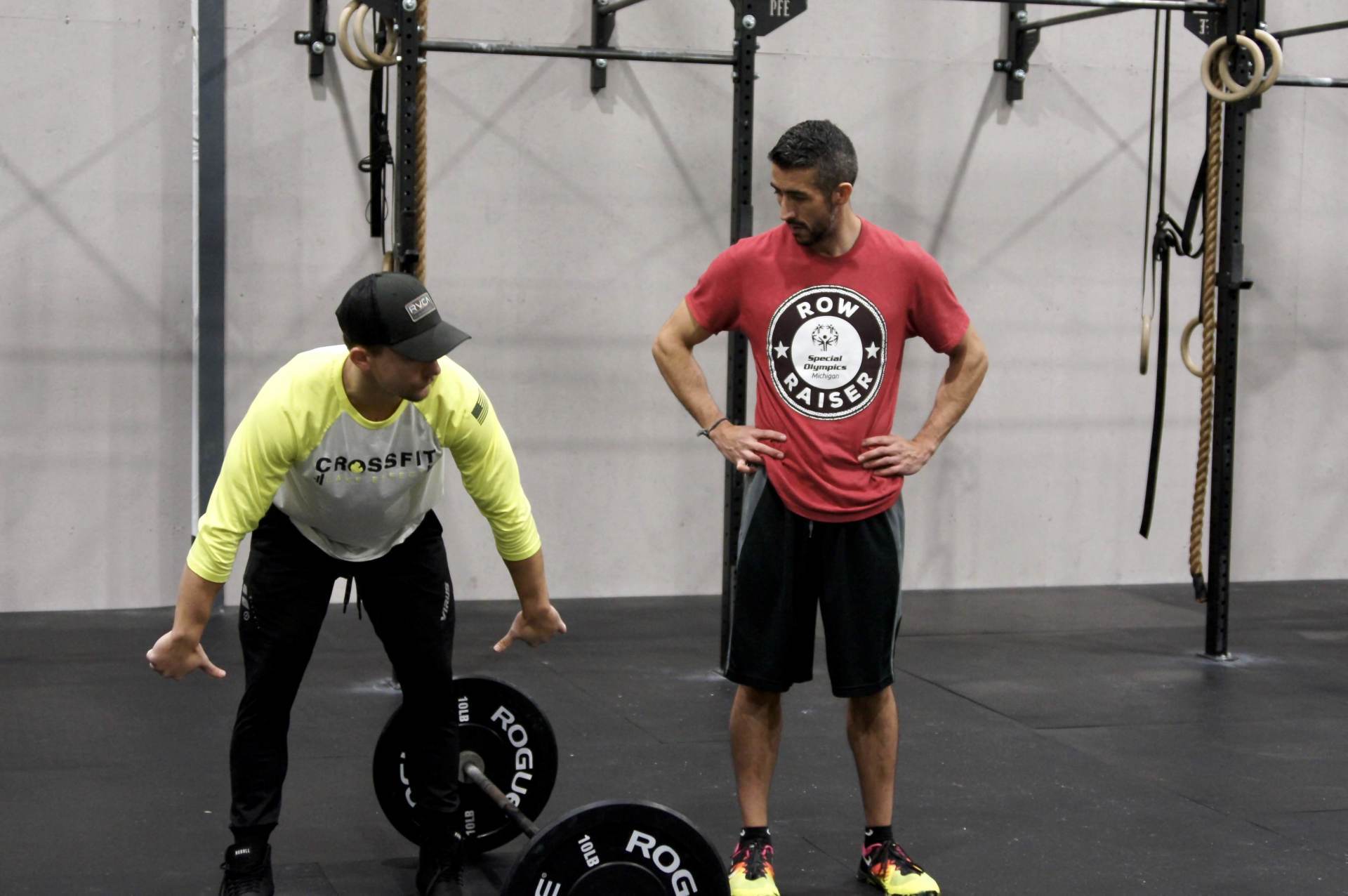 A man in a red shirt is standing next to a man in a yellow shirt in a gym.