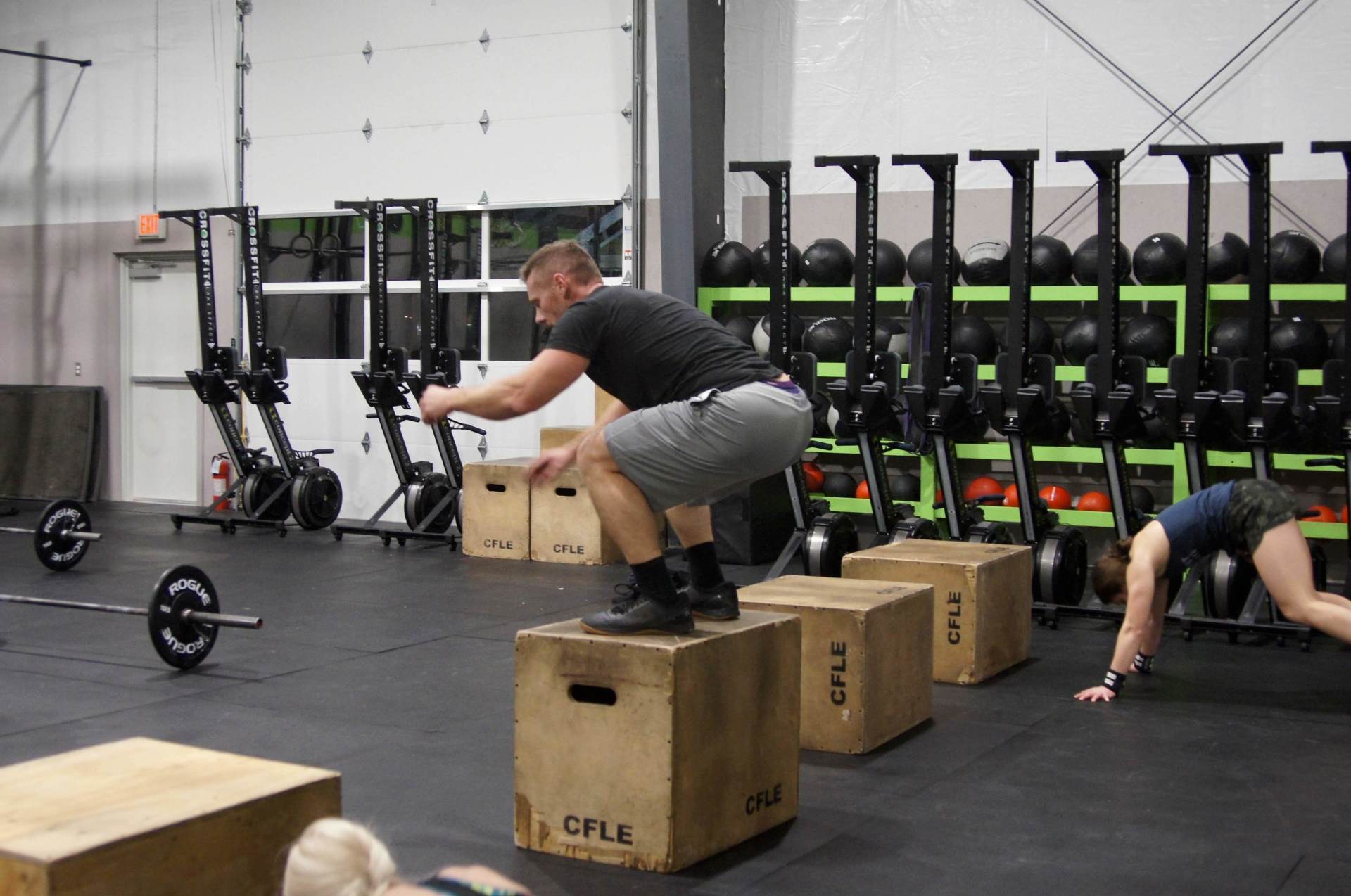 A man is squatting on a box in a gym.