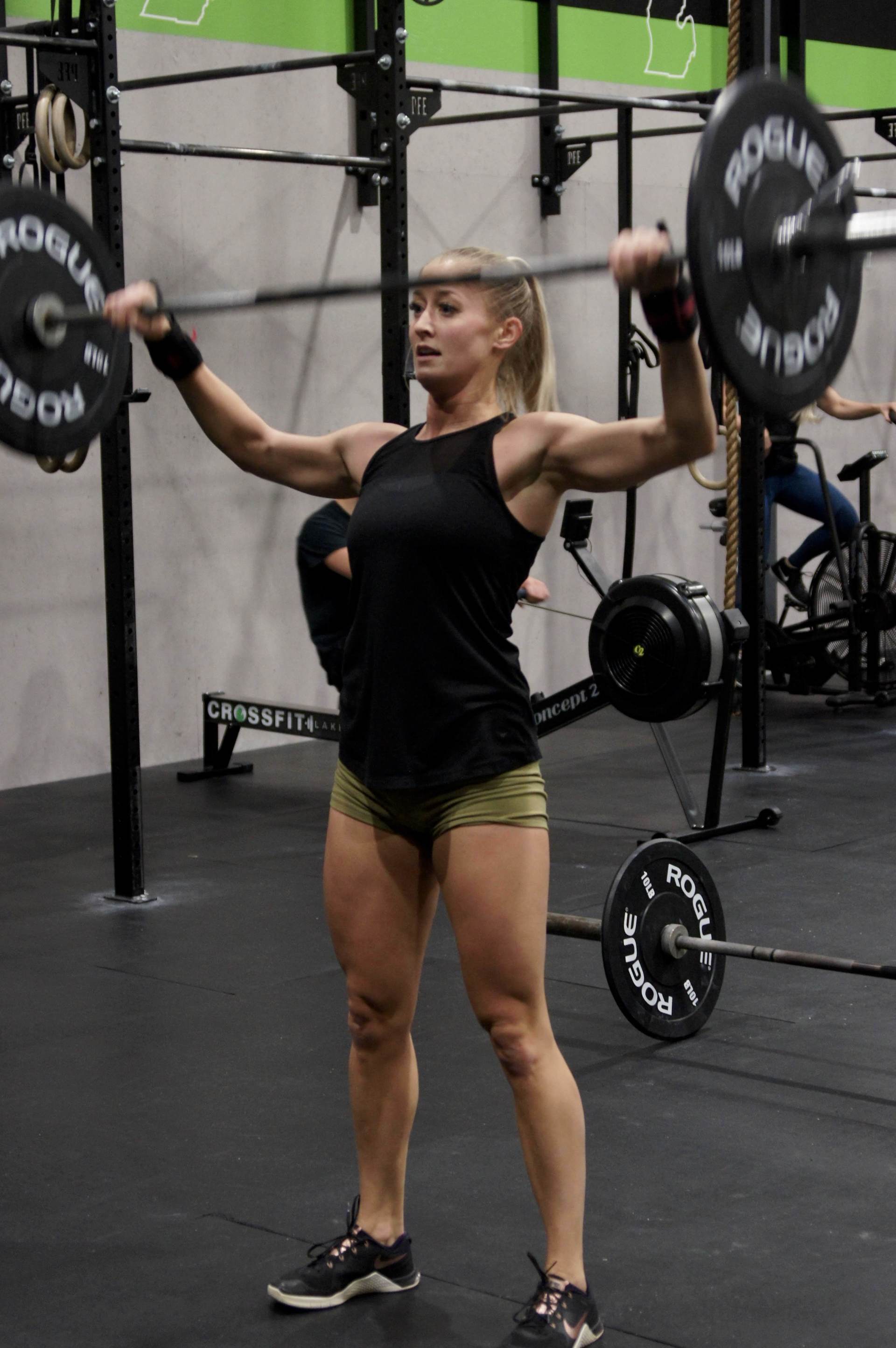 A woman is lifting a barbell over her head in a gym.