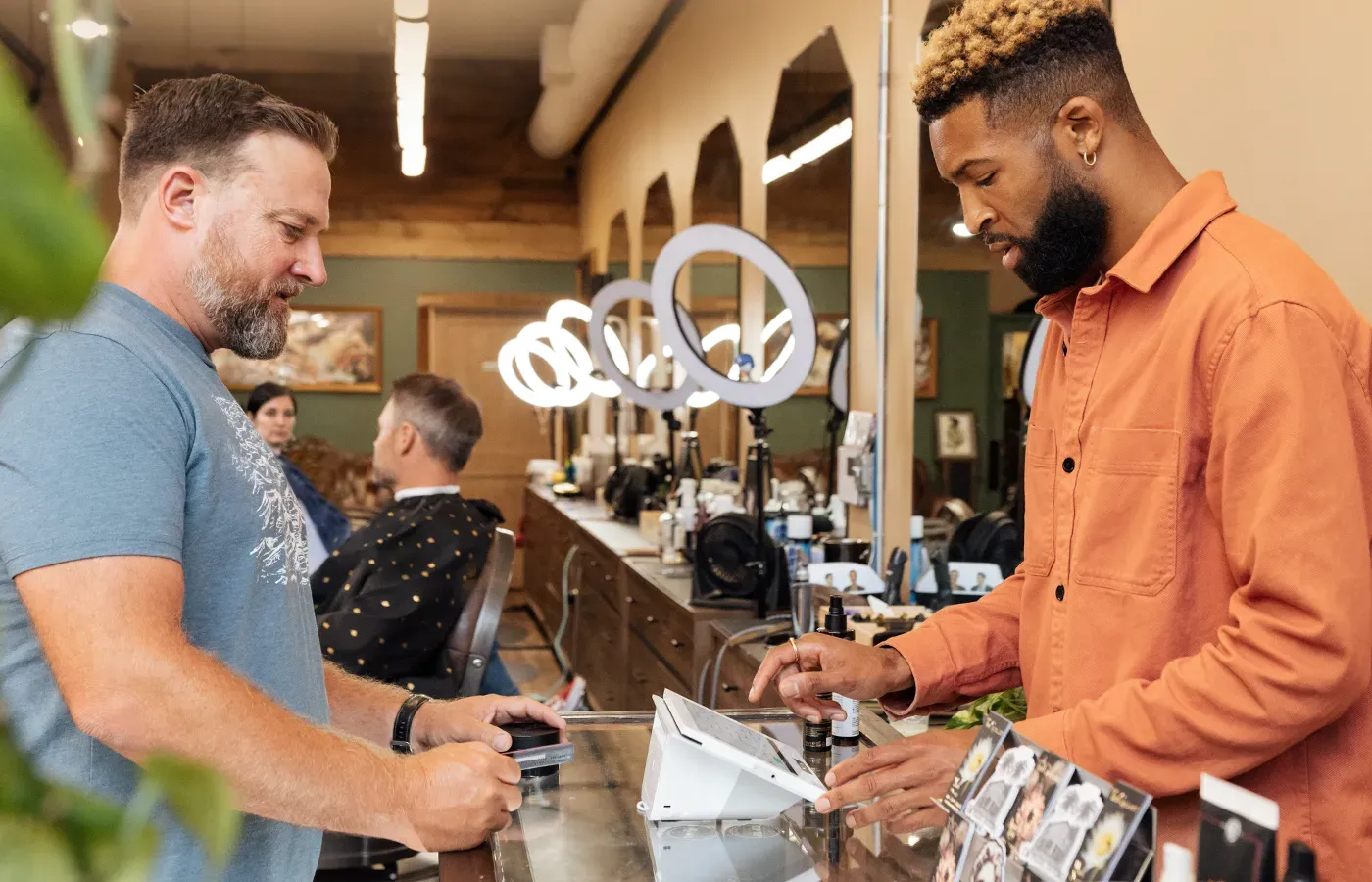 a man is getting his hair cut by a barber in a barber shop and paying for it .