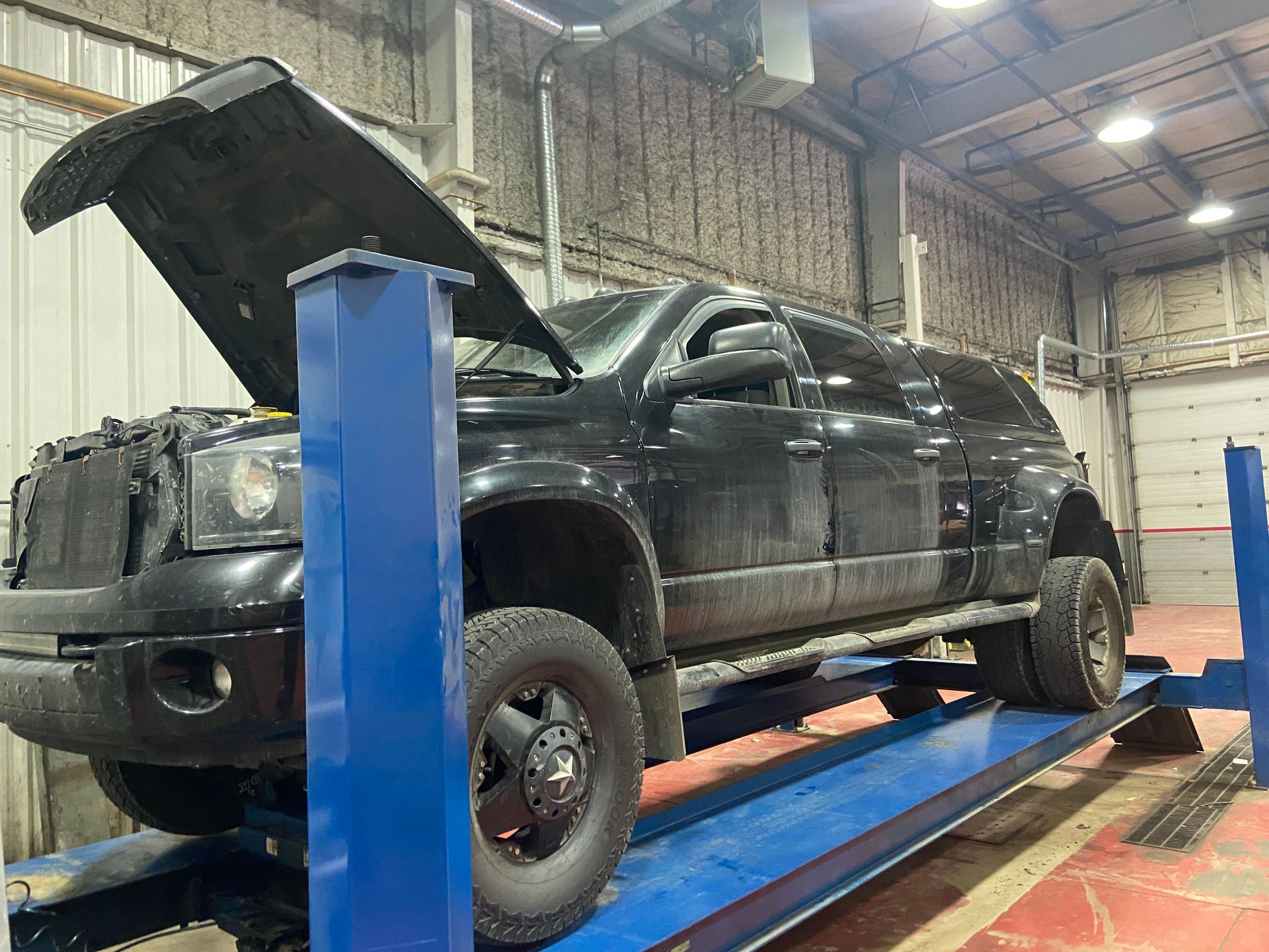 A black truck with its hood up is on a lift in a garage | Cetus Automotive Repair Centre