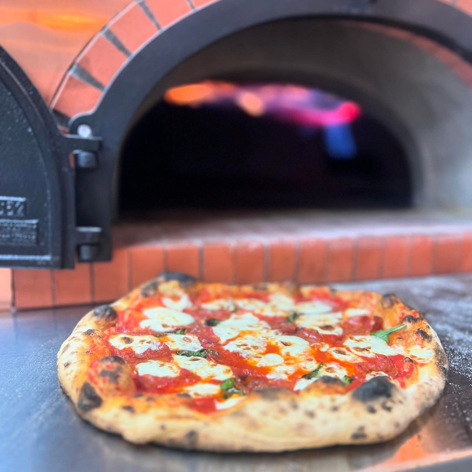 A pizza is sitting on a table in front of a pizza oven