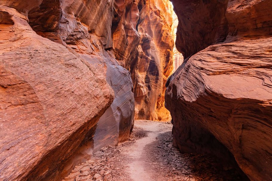 Narrow red sandstone canyon with sunlit rocky walls and a sandy path