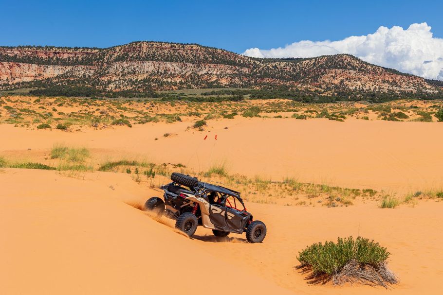 Off-road buggy driving through orange desert dunes with mountains in the background