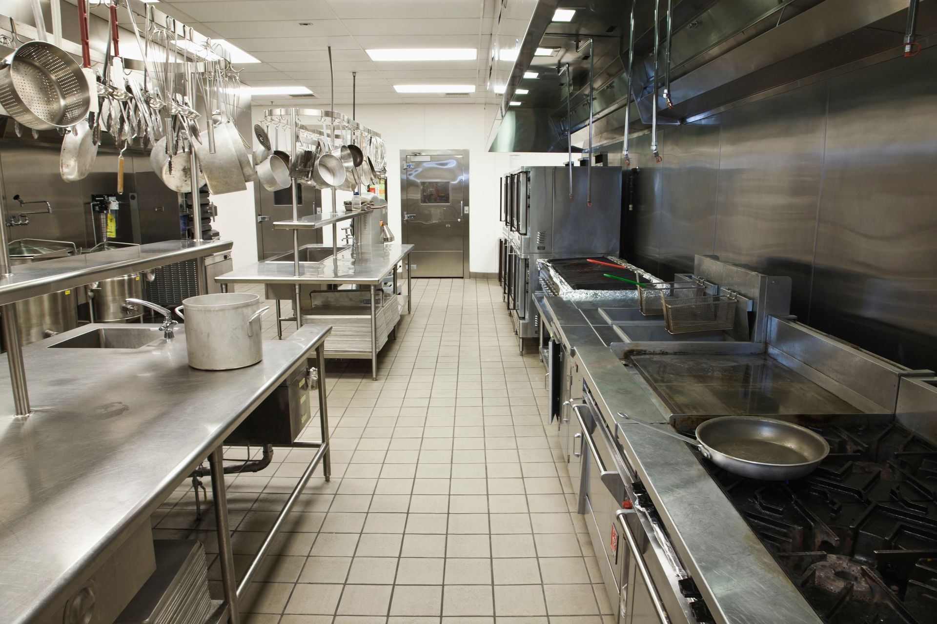 Empty commercial kitchen with stainless steel counters and hanging utensils.