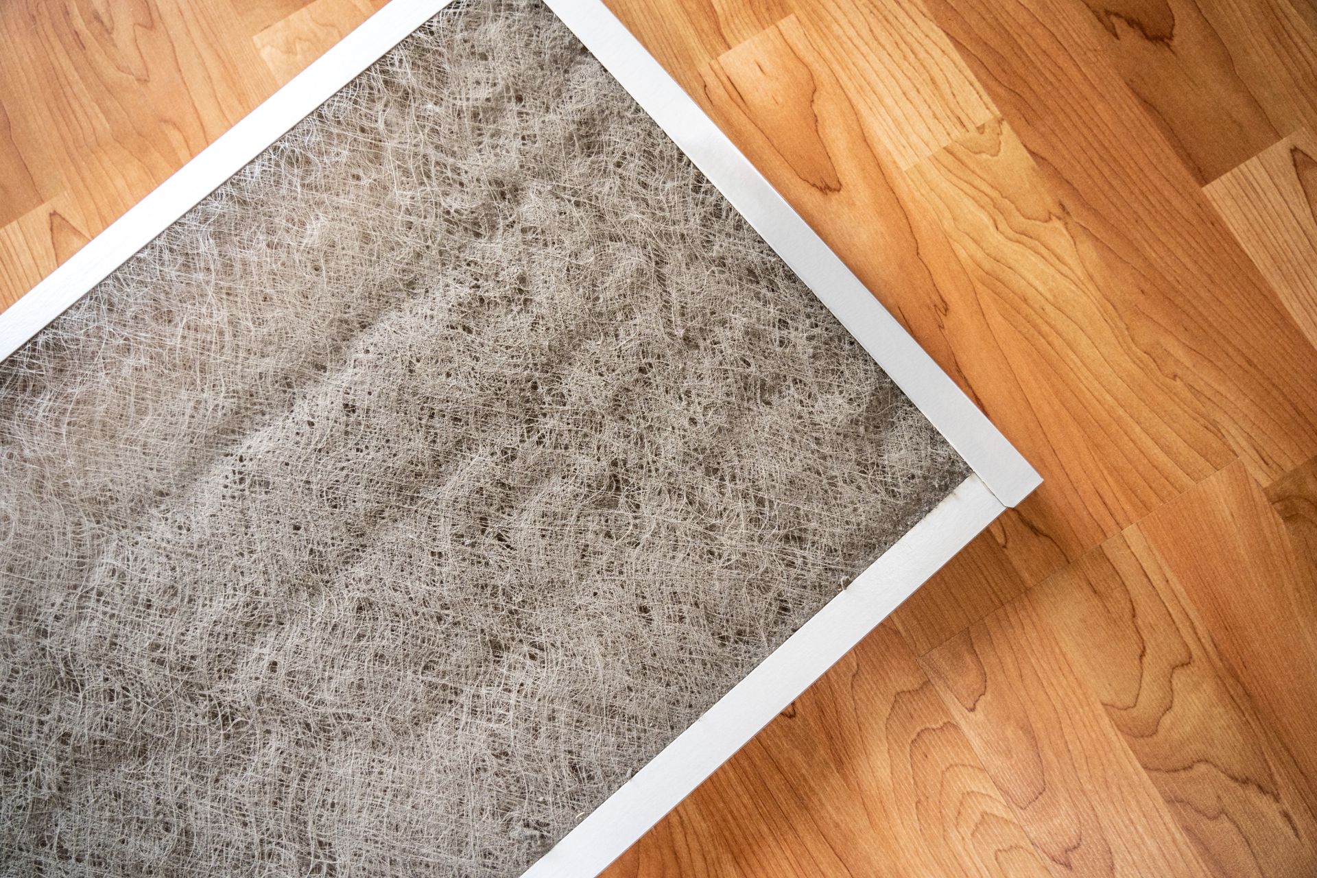 Dirty home air filter covered in dust and lint lying on a wooden floor. Dirty home air filter covered in dust and lint lying on a wooden floor.
