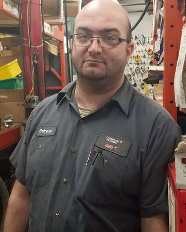 Eric Belrose wearing glasses and a name tag is standing in a warehouse.