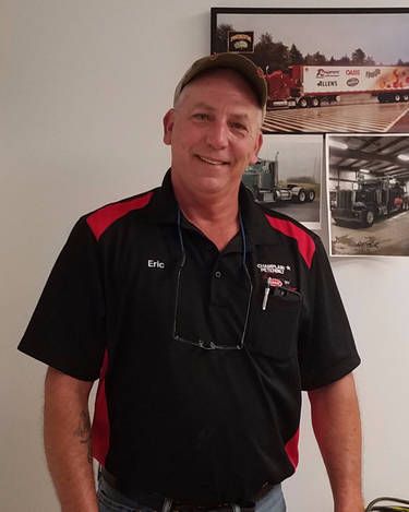 Eric Robideau in a black and red shirt is standing in front of a picture of a truck.