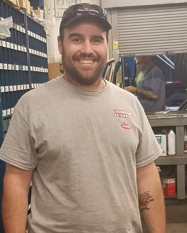 Gabe Mahoney wearing a gray t-shirt and a hat is standing in a garage.