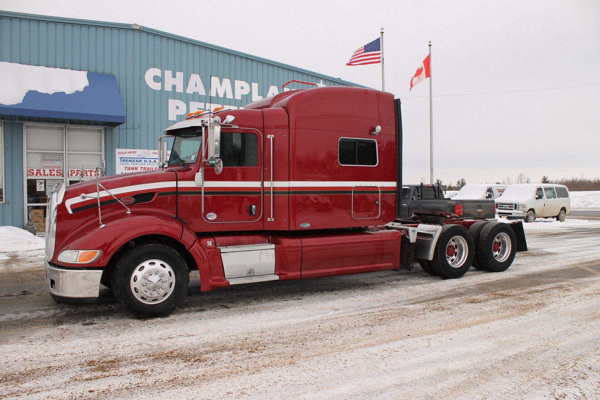 A red semi truck is parked in front of a building that says champlain