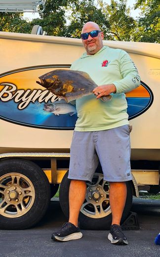 A man is holding a large fish in front of a boat trailer.