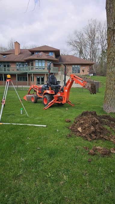 A man is driving a tractor in a grassy field in front of a house.