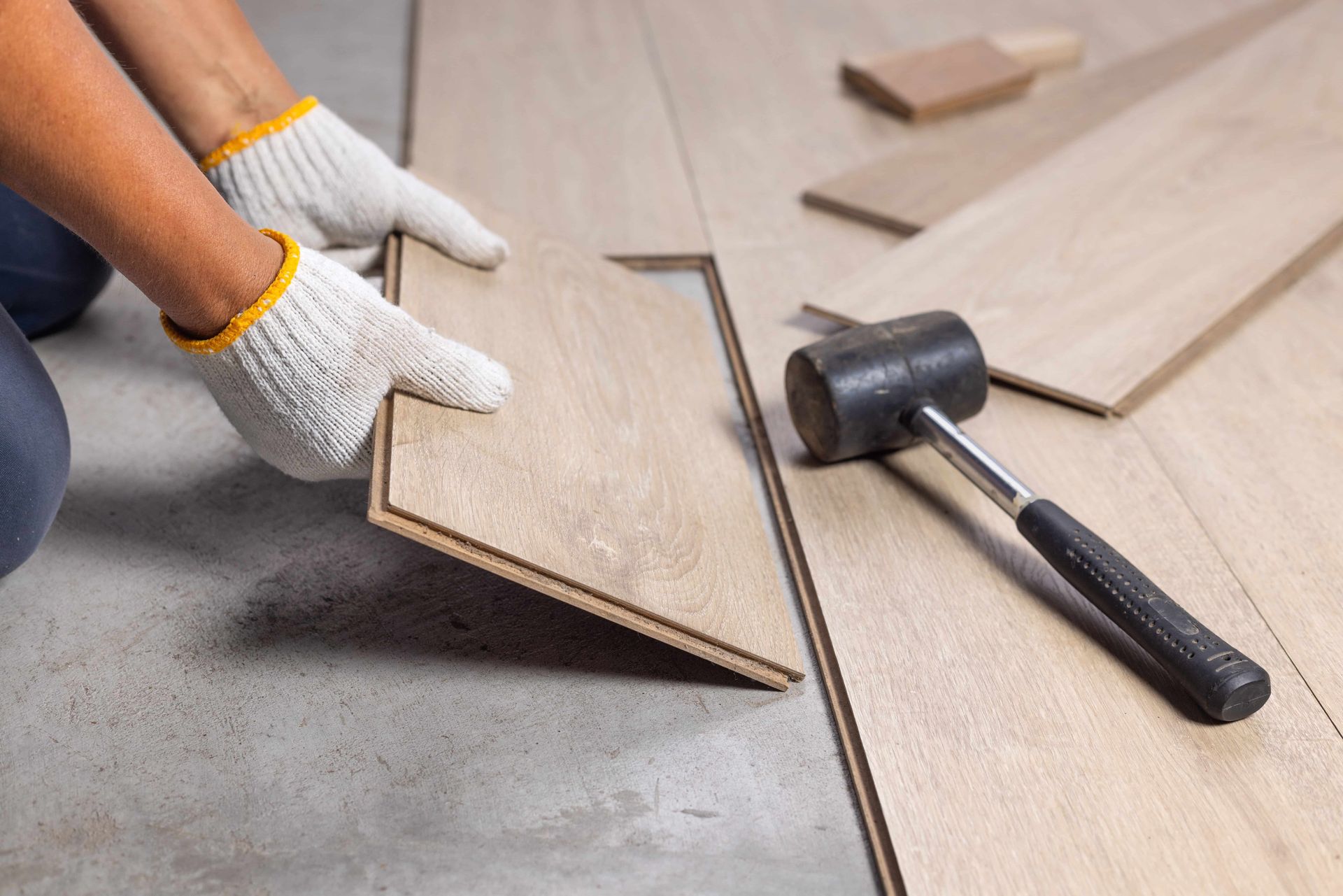 Person wearing gloves installing wooden floor planks with a mallet.