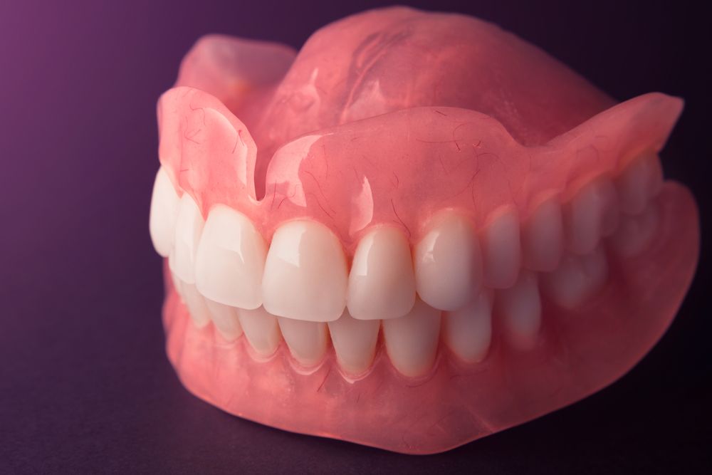 A Close Up of a Denture With White Teeth on a Purple Background — Goonellabah Denture Clinic in Evans Head, NSW