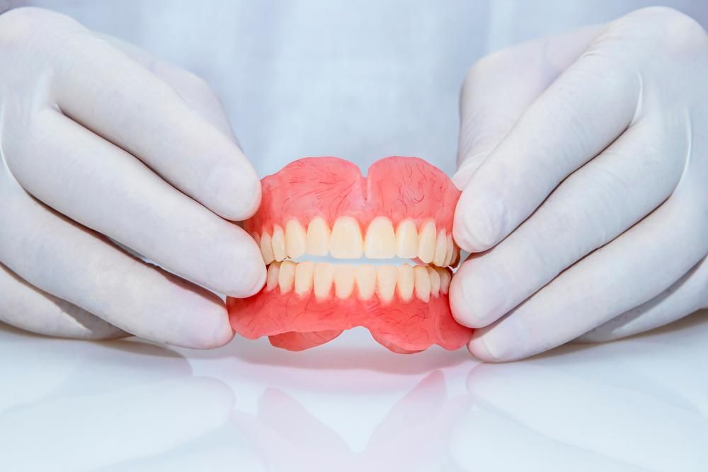A Dentist Holding a Denture — Goonellabah Denture Clinic In Kyogle, NSW