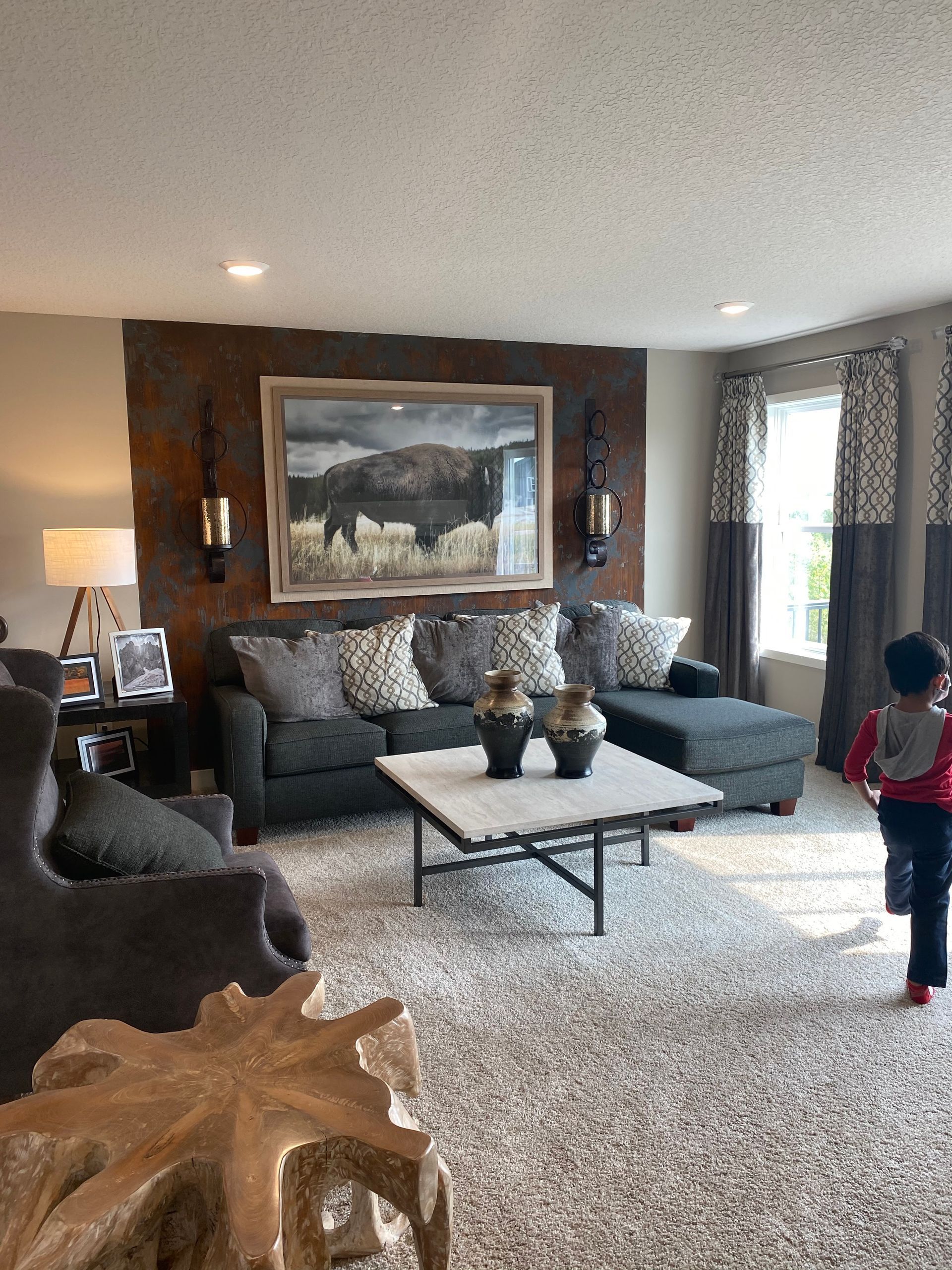 Living room with gray sofa, coffee table, and artwork; person standing near window.