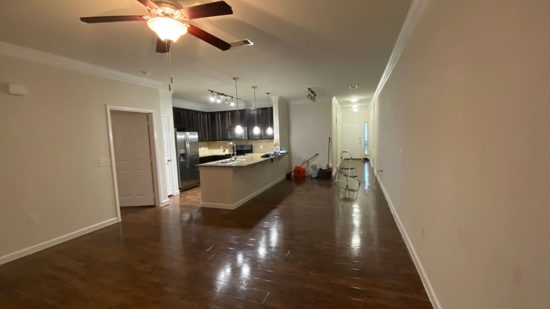 An empty living room with a ceiling fan and a kitchen in the background.
