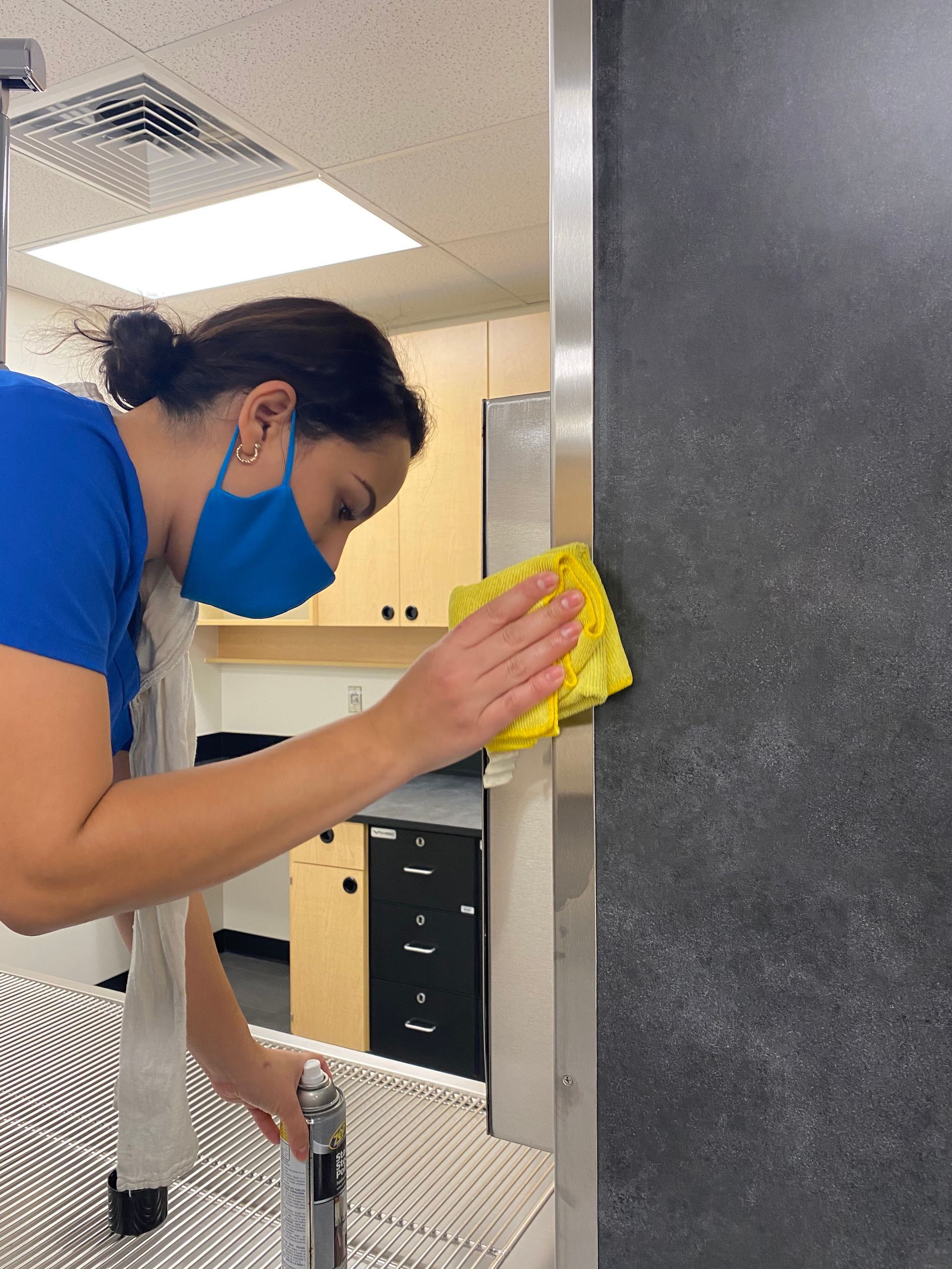 A woman wearing a blue mask is cleaning a door with a yellow cloth.
